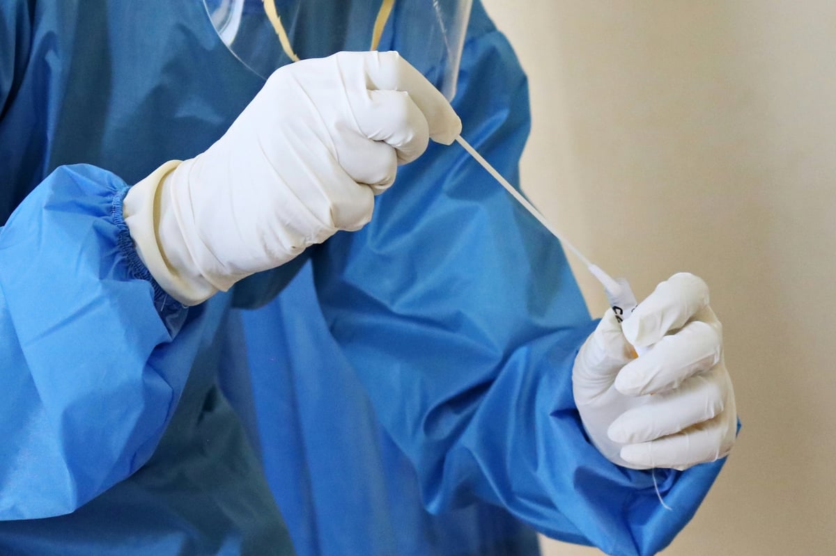 Healthcare worker in blue scrubs and white gloves wrapping a patients injured hand with white medical bandage